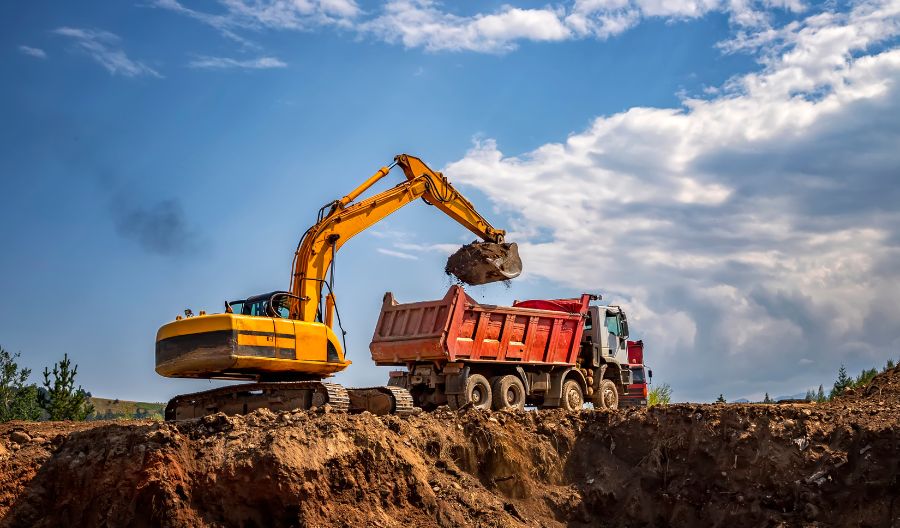 backhoe dumping dirt into a dump truck