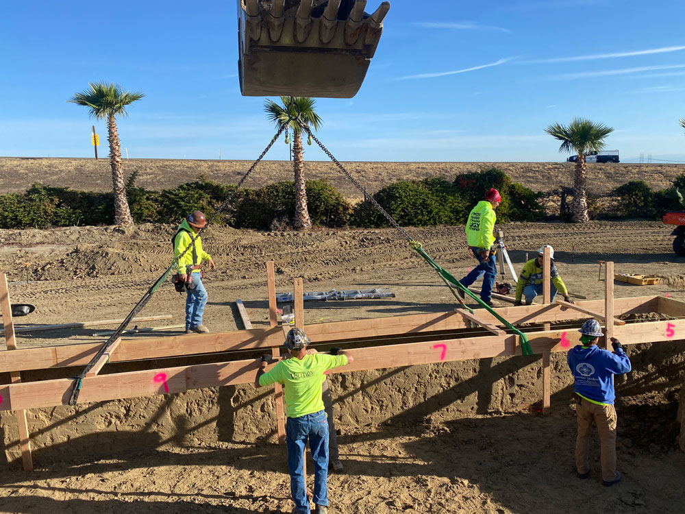 construction workers lowering framing into excavated hole with the help of heavy equipment